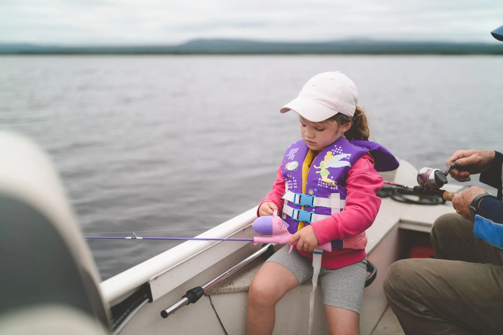 A young girl in a life jacket fishing on a tranquil lake, enjoying leisure time.